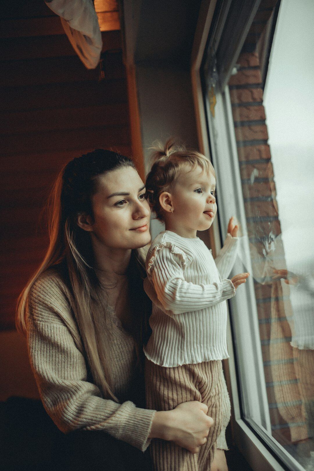 Mother holding her toddler close indoors near a window